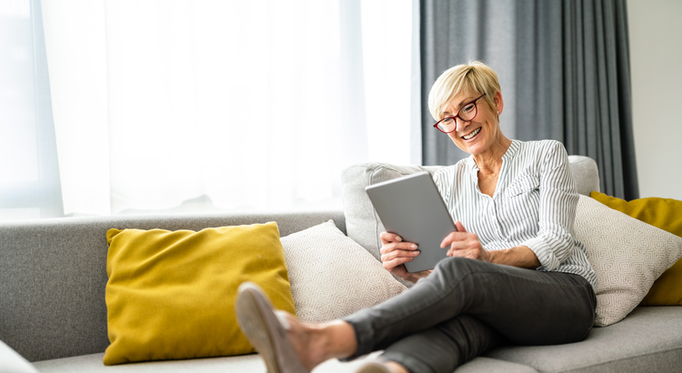 Woman sitting on couch holding and smiling at electronic device
