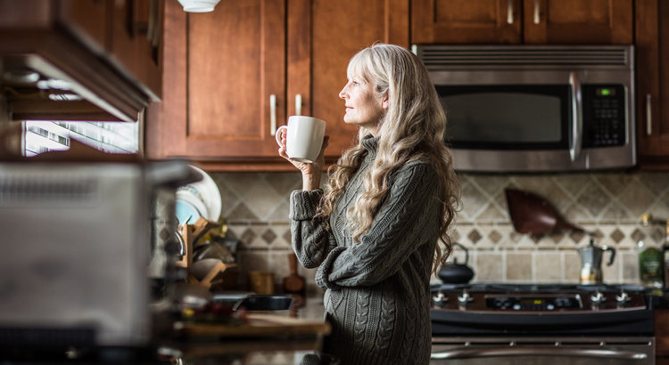 This is a picture of a woman in her kitchen holding a coffee cup. She is thinking about calling Realtor Michael Mahoney in Boston about selling her as she reaches the Baby Boomer Years. 