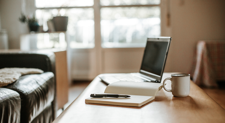 Photo of a coffee table with a laptop, pad and pen. A person is getting ready to work on their finances. 