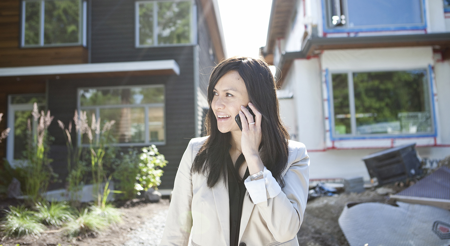 Real estate agent standing near house talking on cell phone