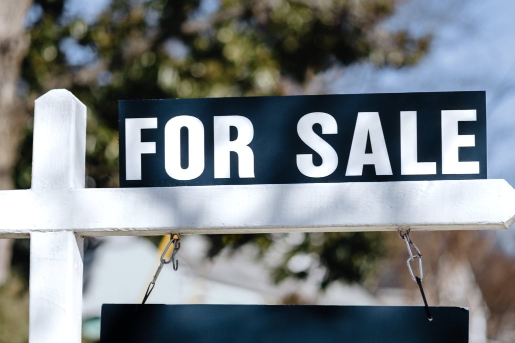 For Sale Sign Hangs in Front Yard of House