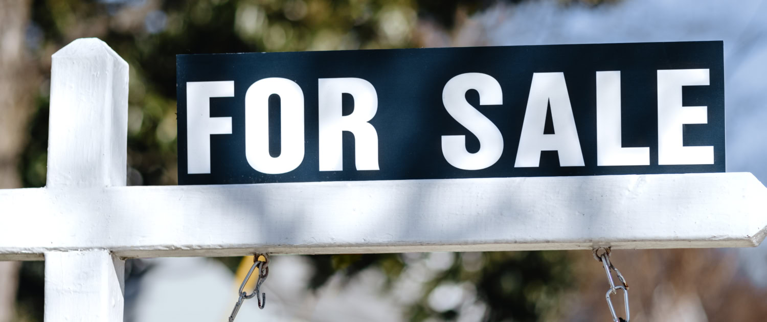 For Sale Sign Hangs in Front Yard of House